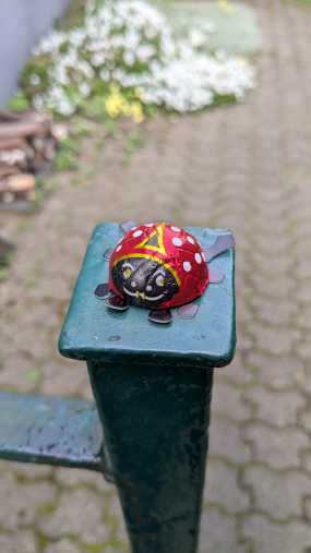 Ein Glückskäfer aus Schokolade liegt auf einem Pfosten des Gartentors