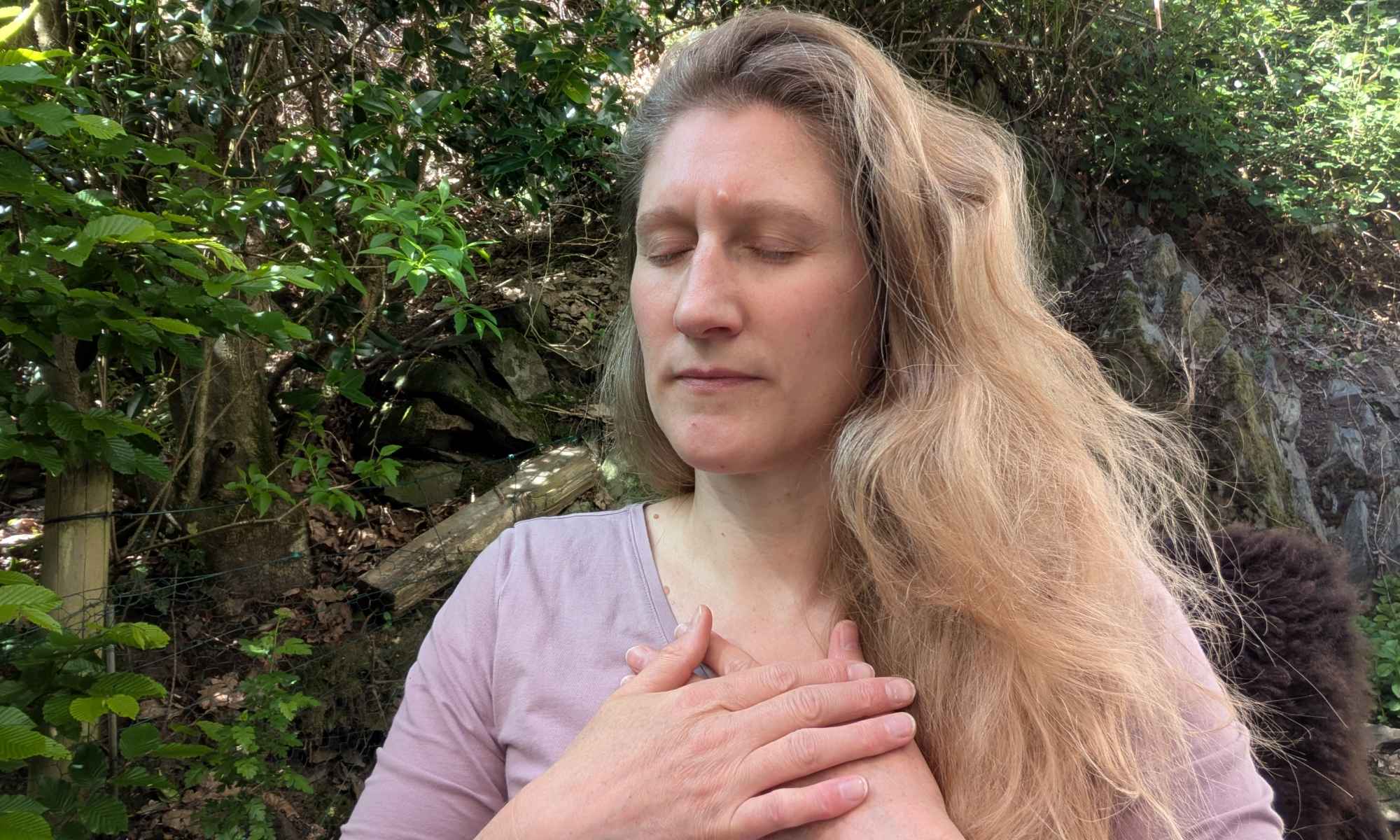 Dorothee sitzt mit geschlossenen Augen und den Händen vor dem Oberkörper in einer meditativ versunkenen Stimmung auf der Terrasse