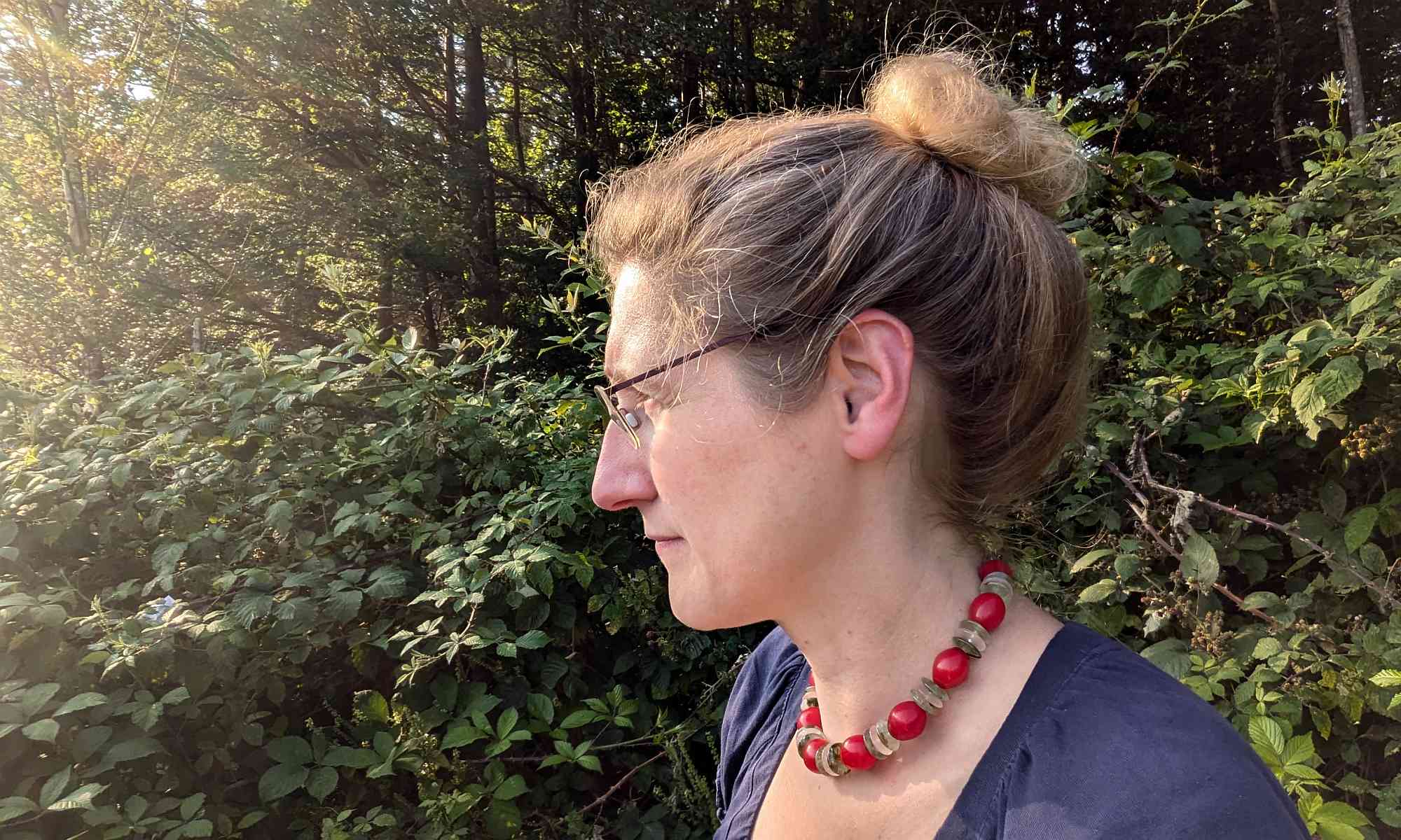 Dorothees Portrait seitlich fotografiert, wie sie am Waldrand in Richtung Sonne schaut