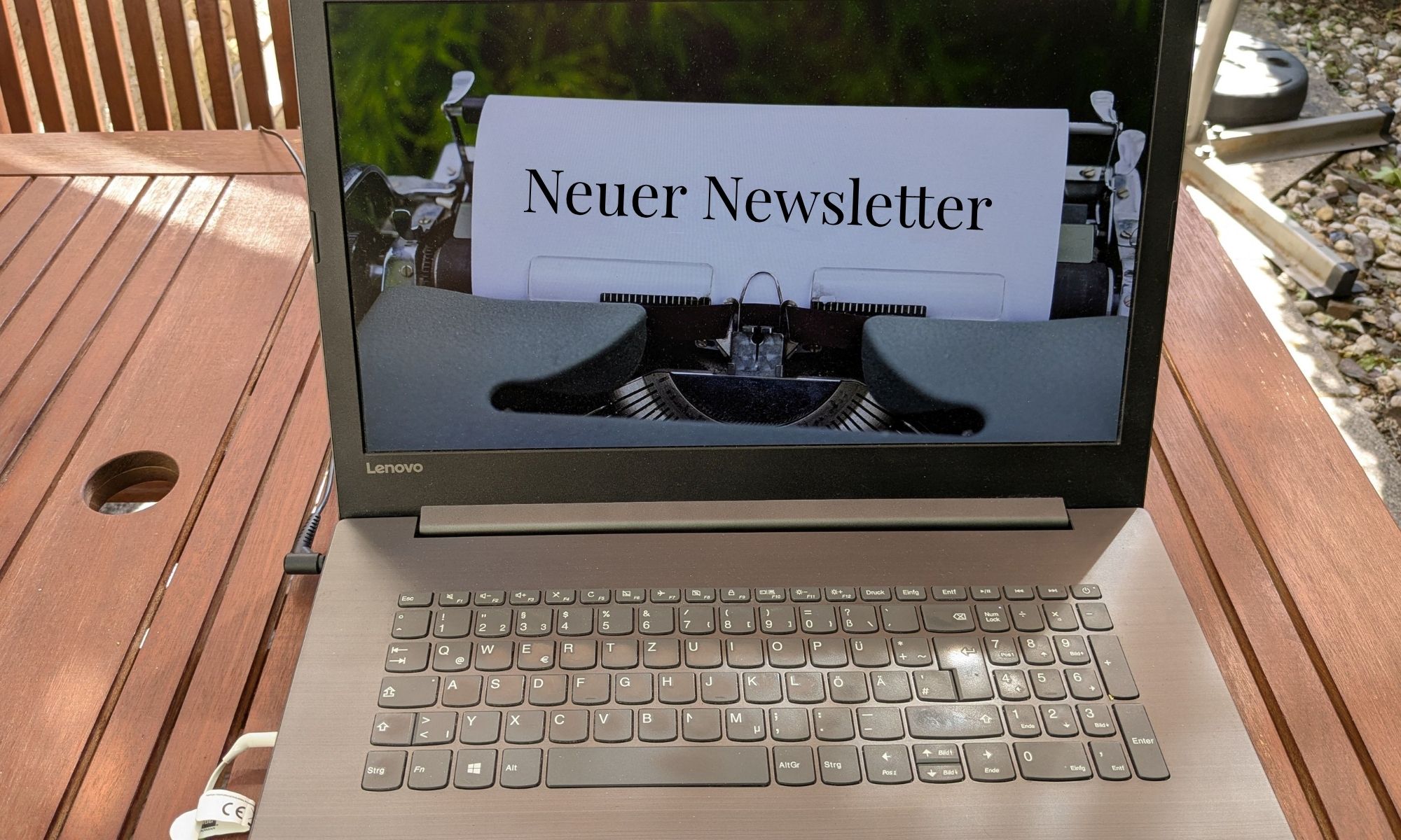 Ein Laptop auf einem Tisch, auf dem Bildschirm steht auf einem Papier Neuer Newsletter. Das Papier ist in eine Schreibmaschine eingespannt