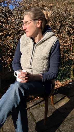 Dorothee sitzt mit Kaffeebecher in der Hand in der Sonne auf der Terrasse