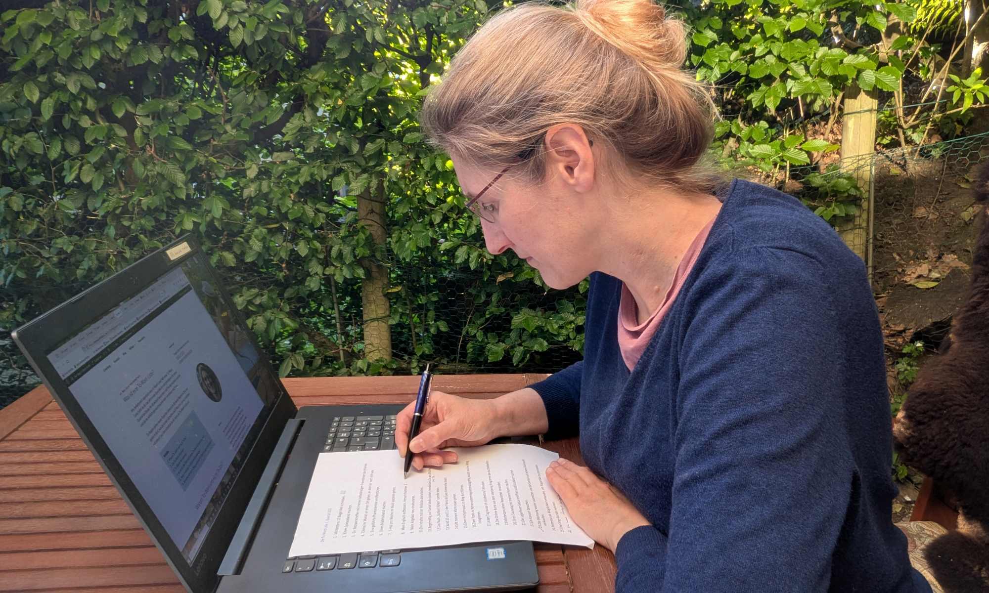 Dorothee sitzt am Laptop mit Zettel und Stift und überlegt die nächsten Inhalte für ihr Content Marketing