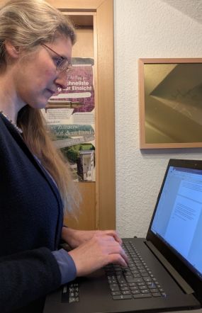 Dorothee steht am Laptop mit redaktionellen Aufgaben.